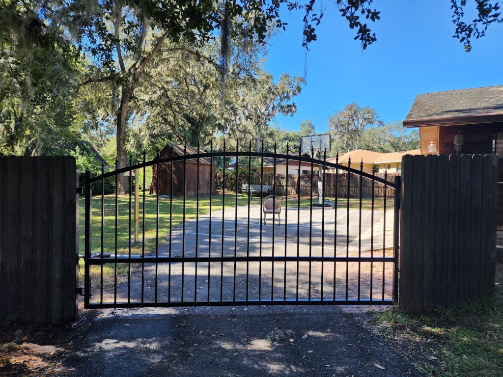 Arched black steel security gate across a wooded driveway