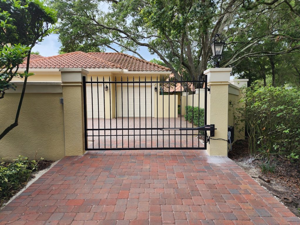 Custom dual driveway gate between stucco pillars on a brick paver drive